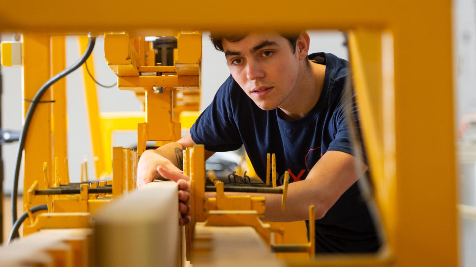 A young man working with a yellow wood machinery.